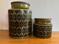 Two green Hornsea Heirloom pattern ceramic canisters with original wooden lids shown front and side by side.