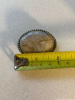 Close-up showing brooch size next to measuring tape, approximately 3.5 cm wide.