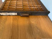 Wooden type set drawer showing multiple small compartments for holding type letters, with a metal pull handle and label '12 Chatt Bold'.