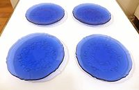 Four cobalt blue glass side plates on white surface