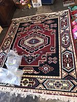 Top view of Turkish style area rug showing central medallion design with geometric motifs in red, black, cream, blue colors with fringe edges.