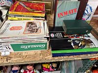 Photo showing stacked Gun Digest magazines, a book titled 'INMATE', and various other books and albums on a wooden shelf.