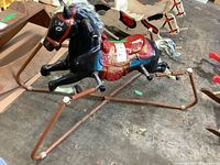 Full view of the black molded resin rocking horse with a red and gold saddle on a rusty metal spring-loaded base.