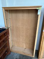 Front view of wooden cabinet, open with empty interior showing shelf support pins attached along vertical sides.