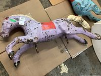 Full side profile of purple enameled metal carousel horse on cardboard background