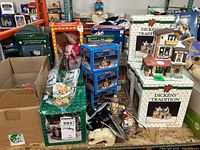 Entire lot arranged on table showing boxed Dickens' Tradition village buildings, musical doll, and various accessories including figurines and decorations.