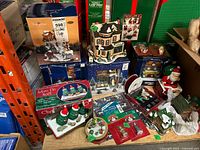 Wide view of multiple Christmas village buildings, ceramic accessories, boxed items, ribbon and utensils arranged together on shelving