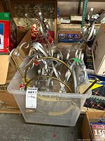 Plastic bin containing metal deer art sculptures and gold-colored metal French horn decorations, placed on a table with boxes in the background.