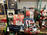 Shelf displaying boxed Christmas village buildings, decorative glasses in box, and various holiday figurines and collectibles