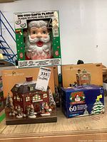 Shows lot contents including a large Santa electronic plaque, two Christmas Village ceramic houses, and a box of 60 outdoor miniature Christmas lights.
