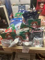 Tray of assorted Christmas village accessories in original packaging, showing different packaging brands and types of figurines and decorative pieces.