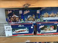 Shelves with boxed Zellers brand Christmas village porcelain buildings, horse carriage, and accessories, labeled with prices.