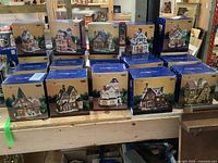 Front view of two rows of six boxed Trim Shoppe village houses on wooden bench