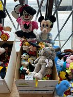 Box containing assorted Disney plush and plastic toys including Minnie Mouse and baby Mickey Mouse plush figures and small plastic Disney character toys.