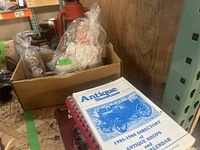Cardboard box containing vintage dolls, one wrapped in plastic with a tag showing 9 inches height, along with antique reference books.