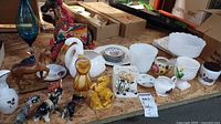Photo of assorted animal figurines including horse, elephant, dog, owl, mythical creature, and clowns, along with floral plates and small vases.