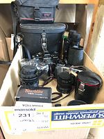 Box and contents overview showing various camera equipment including Praktica B200, lenses, flash unit, and binoculars arranged inside a cardboard box with cases.