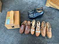 Six pairs of shoes and wooden shoeshine box with shoe stretcher visible on top.