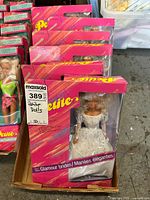 Box containing multiple Petite Glamour Bride dolls in original pink and purple packaging, showing intact labels and visible dolls inside in bridal dresses.