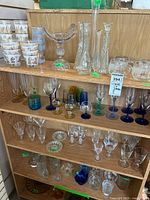 Shelf displaying an extensive variety of glassware including stemware, colored glasses, and decorative pieces.