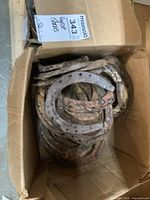 Box containing multiple rusty metal horse shoes stacked and varying in size.
