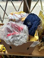 Photo showing a cardboard box holding multiple McDonald's clothing items including a navy blue vest and a red and yellow uniform piece, visible through plastic wrapping.