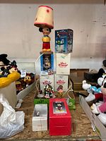 Mickey Mouse lamp, boxed Walt Disney musical figurines, and other Disney collectibles arranged on a table.