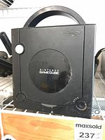 Front view of black Nintendo GameCube with circular lid, handle on back, visible wear and dust.
