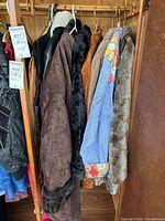 Brown suede coat with fur lining and cuffs, black leather jacket with white collar, black fur vest, brown suede fringed vest, blue denim jacket with colorful lining, gray fur coat hanging in wardrobe