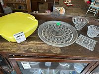 Full view of the lot items displayed on a wooden surface: yellow Pyrex casserole dish with lid, round glass serving plate, clear glass creamer, sugar bowl, and rectangular condiment dish.