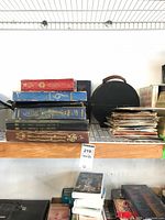 Wide shelf image showing a stack of record albums, black vinyl record case, and a pile of loose 45 RPM records.