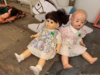 Two vintage dolls sitting on floor in front of wooden sit-in rocking horse