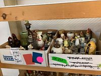 View of two cardboard boxes filled with an assortment of vintage ceramic, glass, and metal salt and pepper shakers in various novelty shapes and styles.