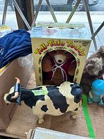 Tell-Tale Teddy cassette player in original box behind black and white cow toy on a wooden surface.