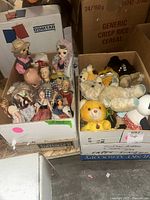 Wide view of the two boxes containing dolls and plush toys, showing several dolls in various outfits on the left and multiple plush toys packed together on the right.