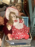 Vintage rag doll dressed in red and white polka dot dress with matching bonnet, sitting among other dolls