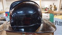 Side view of vintage black fire helmet showing its shape, wear, and glossy finish.