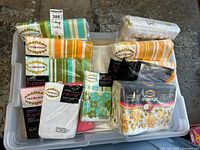 Top view of bin containing several packaged vintage linen sheet sets and pillowcases, showing bright stripes, floral prints, and some white linens, all mainly Tex Made brand.