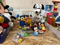 Overview of multiple Disney character toys including Mickey Mouse, Donald Duck bobbleheads, and plush Pongo Dalmatian on a plywood surface