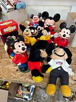 Lot of vintage Mickey Mouse dolls and figurines on wooden surface with cardboard boxes in background.