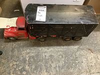 Full view of vintage Tonka Toy livestock transport trailer showing red truck cab attached to black trailer with six wheels, displaying signs of wear and paint chipping.