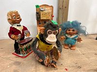 Photo of four vintage toys: mechanical monkey with cymbals, bartender windup toy, Ranch Phone, and blue-haired troll doll on wooden surface.