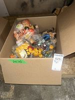 Large cardboard box filled with various plastic toys including Winnie the Pooh and Flintstones figures inside plastic bags.