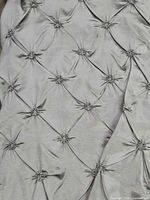 Close-up of silver pinched tufted textile showing details of fabric and gathering points.