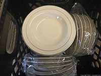 Stacks of white china bowls with thin gold rim trim, some bowls are nested and wrapped in plastic for protection and storage.