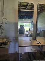 Single double-sided hair station with large rectangular mirror, stainless steel countertop with holes, and drawer below.