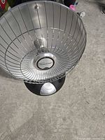 Photo of a Bionaire ReflectaDish space heater sitting on a concrete floor, showing front protective grill and reflective heating element.