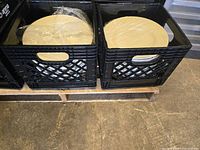 Two black crates holding several large pasta bowls stacked inside, placed on a wooden pallet on a concrete floor.