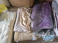 Stack of multiple folded tablecloths in beige, white, tan, and purple colors.