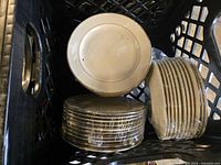 Photo of multiple stacks of ivory plates with gold trim placed inside a crate.